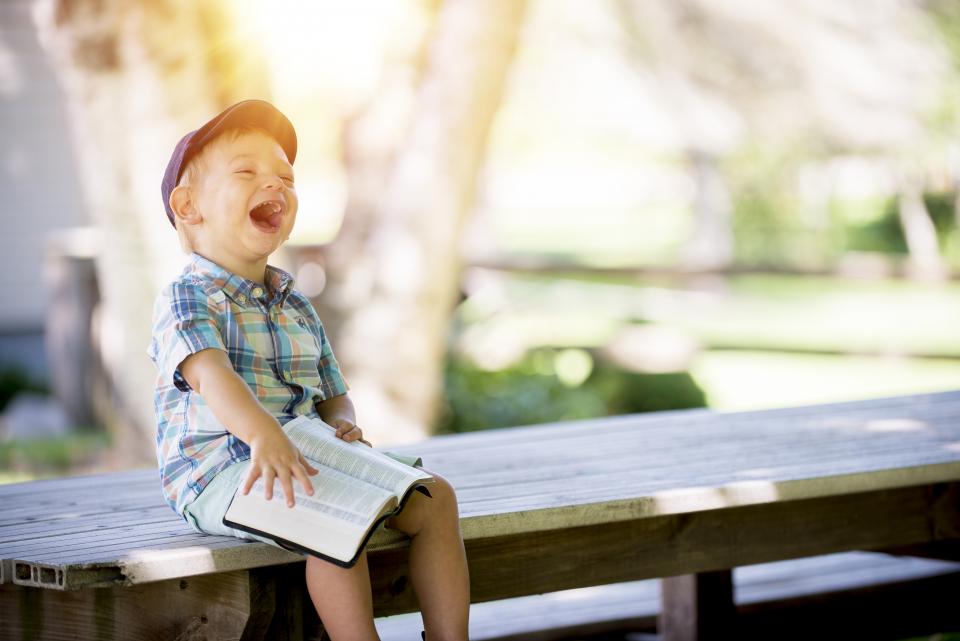 Boy on bench laughing while reading a book