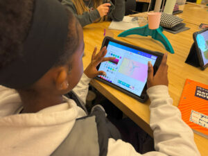 Photo over a student's shoulder where she is working on a tablet. The tablet has color adjustments and a wind turbine image.