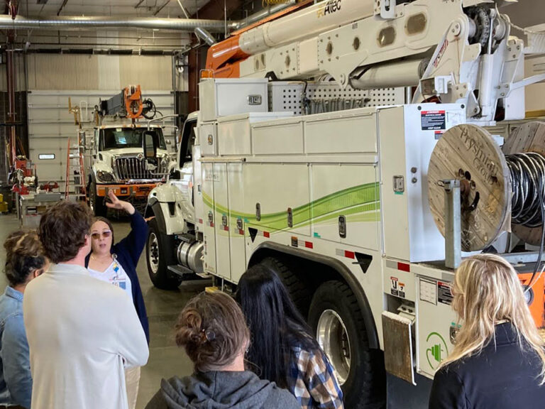 A group of educators look at a power company bucket truck inside a garage.
