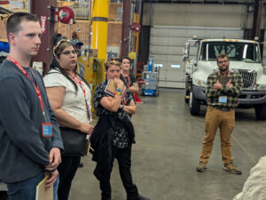 Teachers facing the camera in a large garage. A white utiltiy truck is parked behind.
