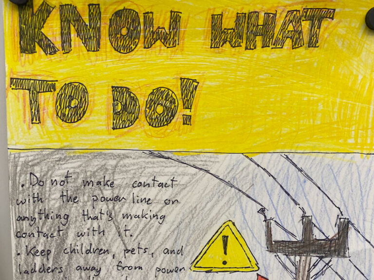 Photo of student PSA, The top half is yellow with big black text that reads "KNOW WHAT TO DO!" Below that the top of a power line and pole can be seen on the right. To it's left is a yellow warning triangle symbol. To the left is the text "Do not make contact with the power line or anything that's making contact with it. Keep children, pets, and ladders away from power"