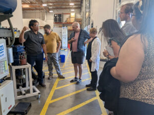 Teachers stand on a concrete floor with yellow marking To the left is a cut-away model of a wind turbine motor .